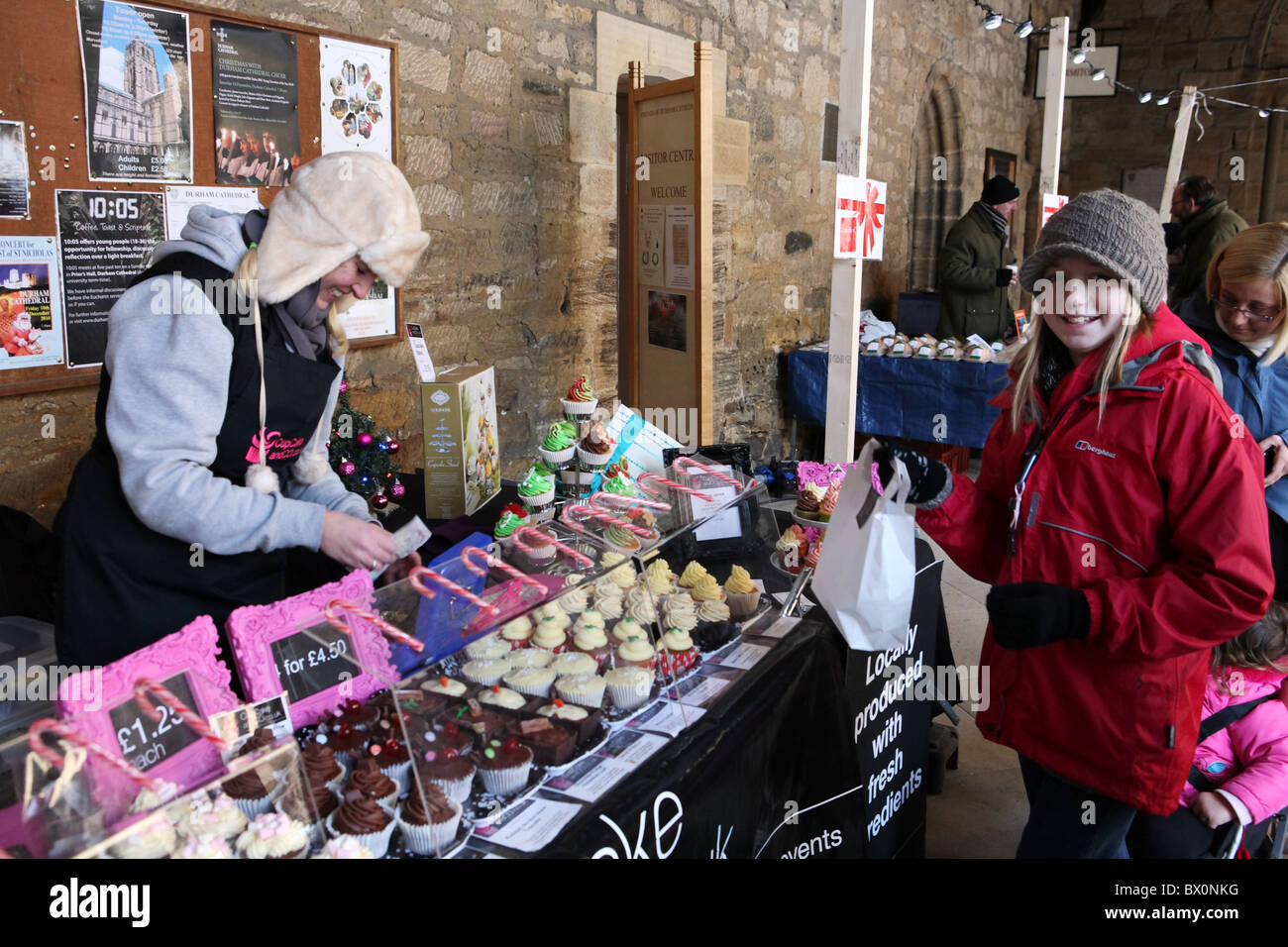 Durham Xmas mercato entro il chiostro della Cattedrale di Durham. Una ragazza acquista prodotti dolciari da questo stallo. Foto Stock