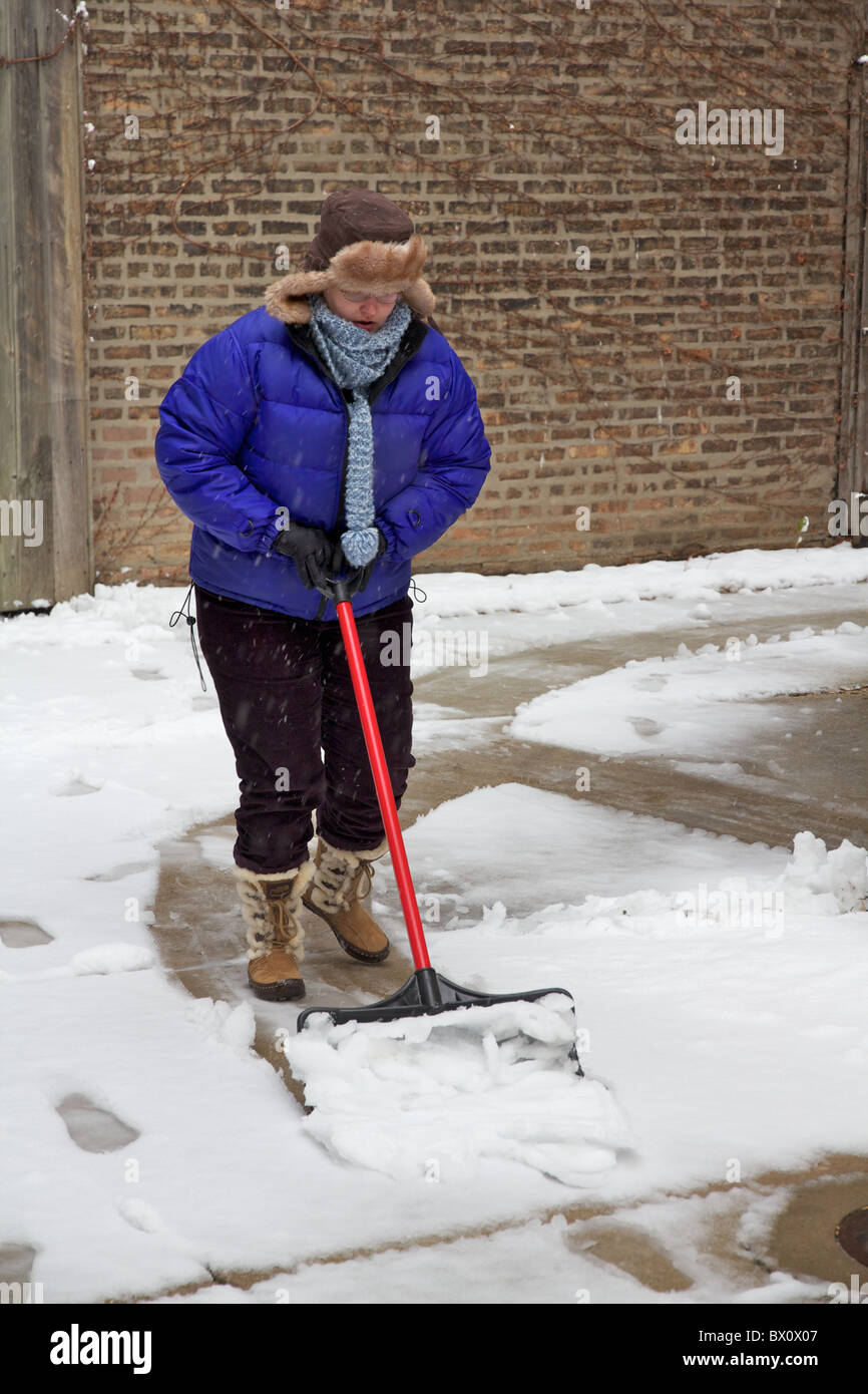 La donna la rimozione di neve dal marciapiede con pala da neve. Foto Stock