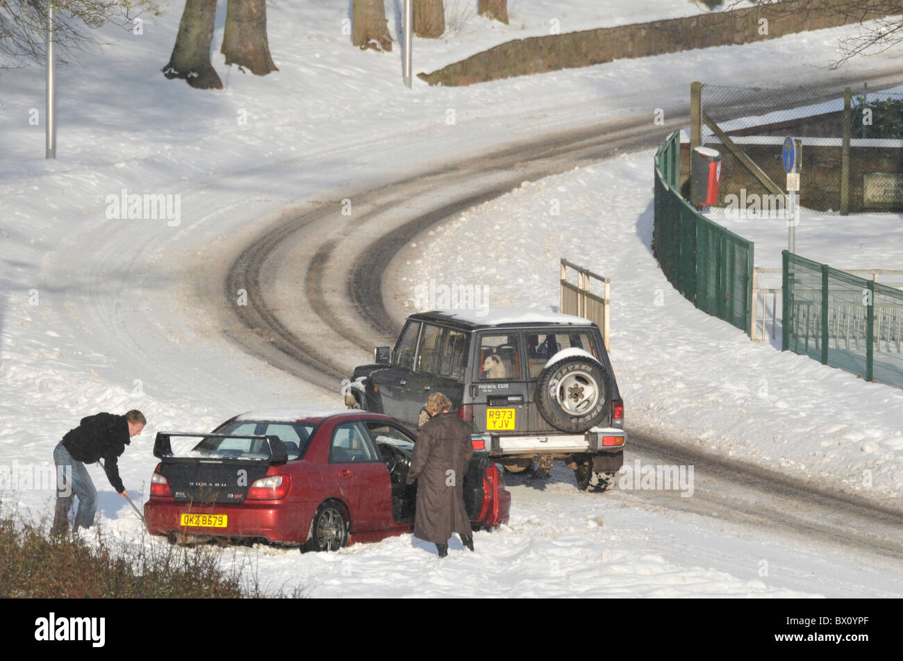 Un giovane uomo cancella la neve da sotto i pneumatici della sua vettura intrappolati nella neve. Foto Stock