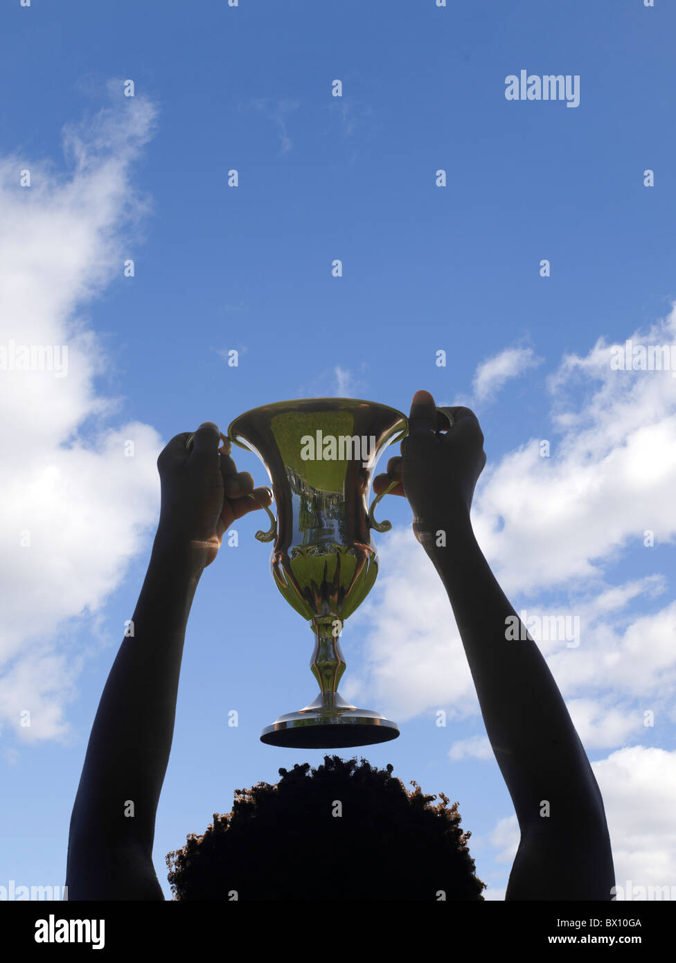 Una persona vittoriosa regge un'ampia coppa di trofei scintillante, sagomata contro un cielo azzurro con poche nuvole. Foto Stock