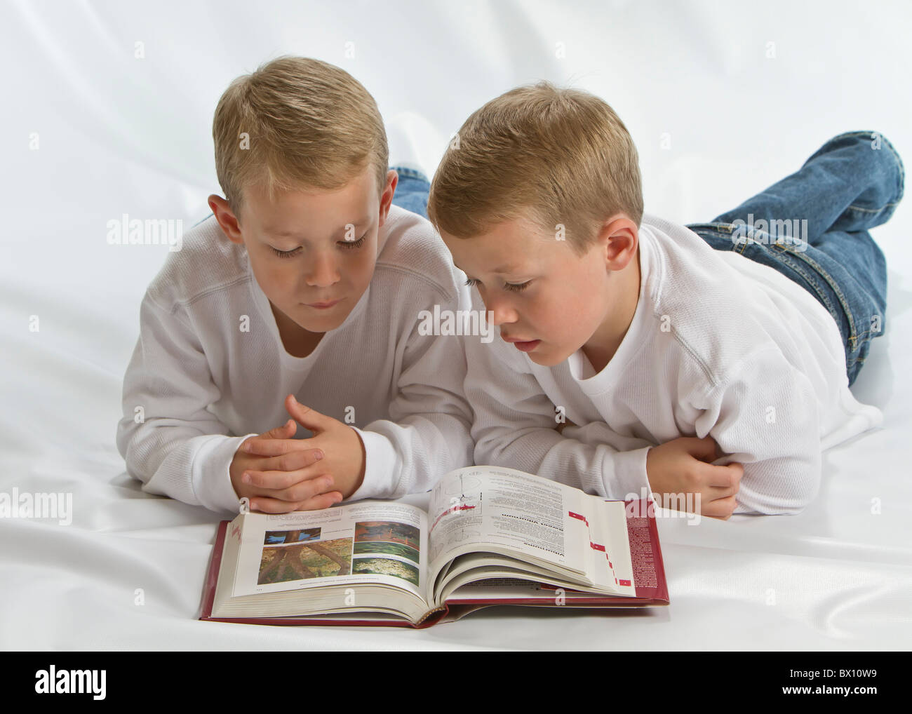 Due dei 6 anni gemelli identici la posa sul pavimento la lettura di un libro Foto Stock