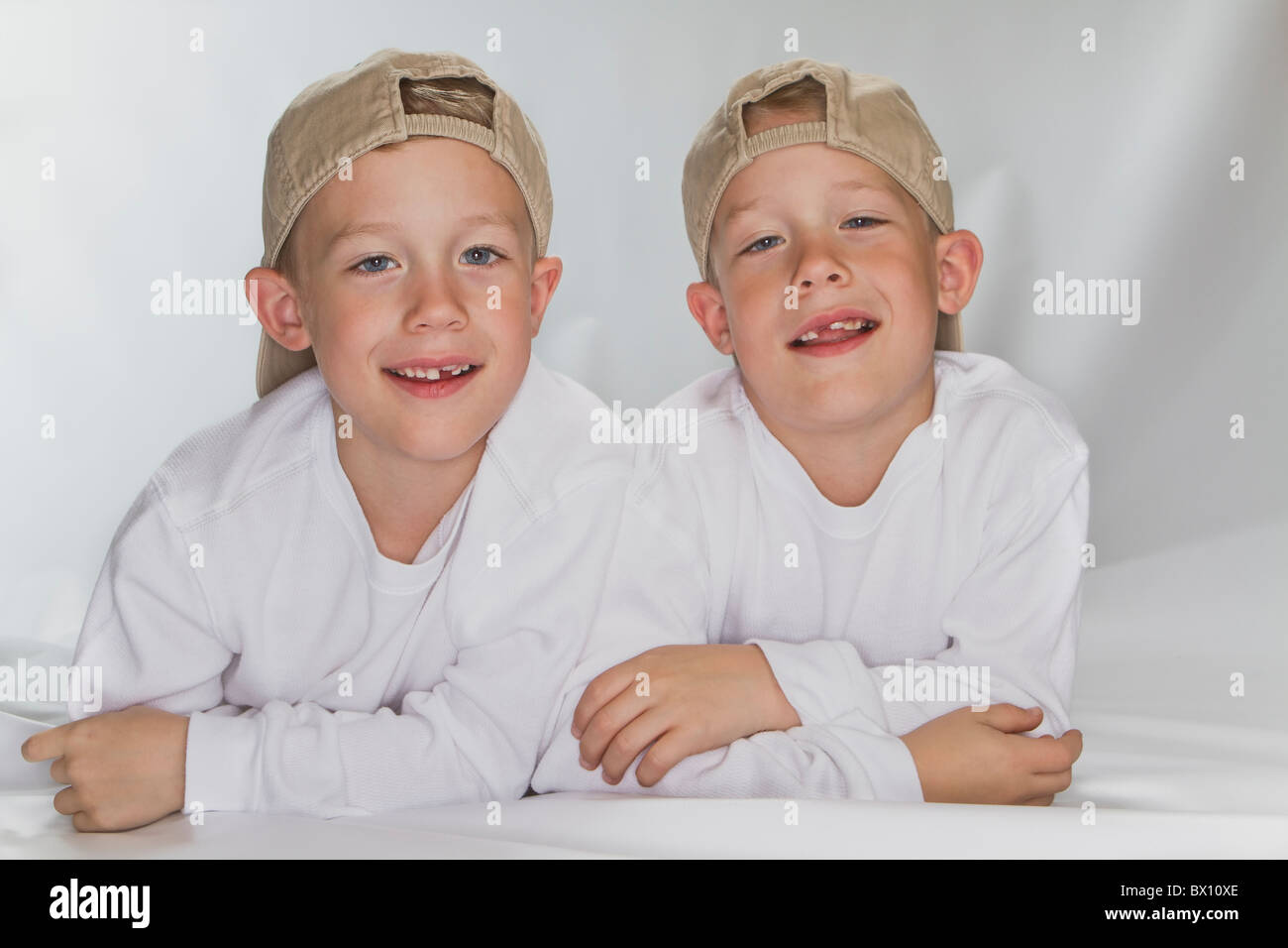 6 anni gemelli identici la posa sul pavimento sorridente indossando un cappello da baseball Foto Stock