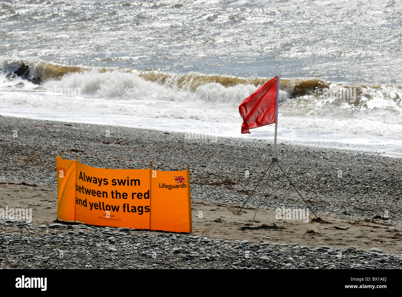 Red Flag di avviso su una spiaggia deserta con mare mosso, Aberystwyth, Galles Foto Stock