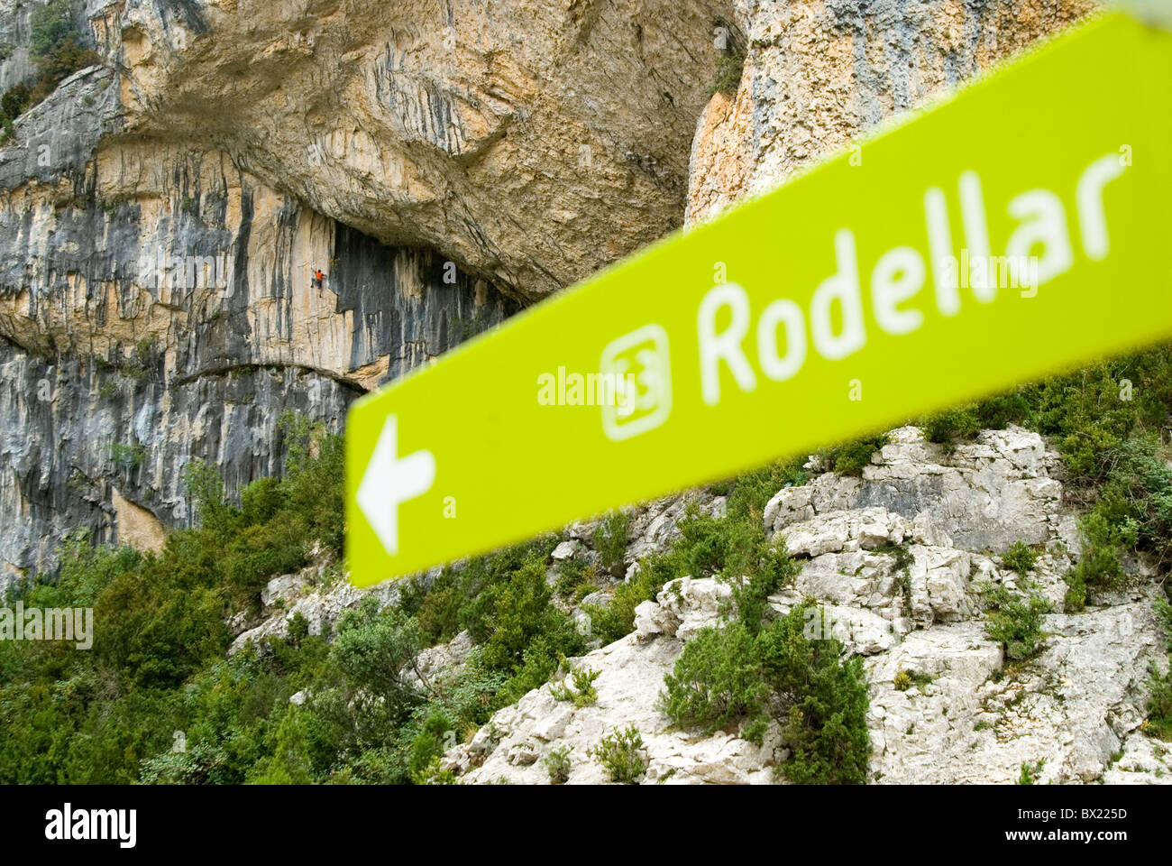 Un cartello verde a Rodellar, Spagna. Un scalatore in background la scalata su roccia a strapiombo cliffs, cespugli verdi intorno a. Foto Stock
