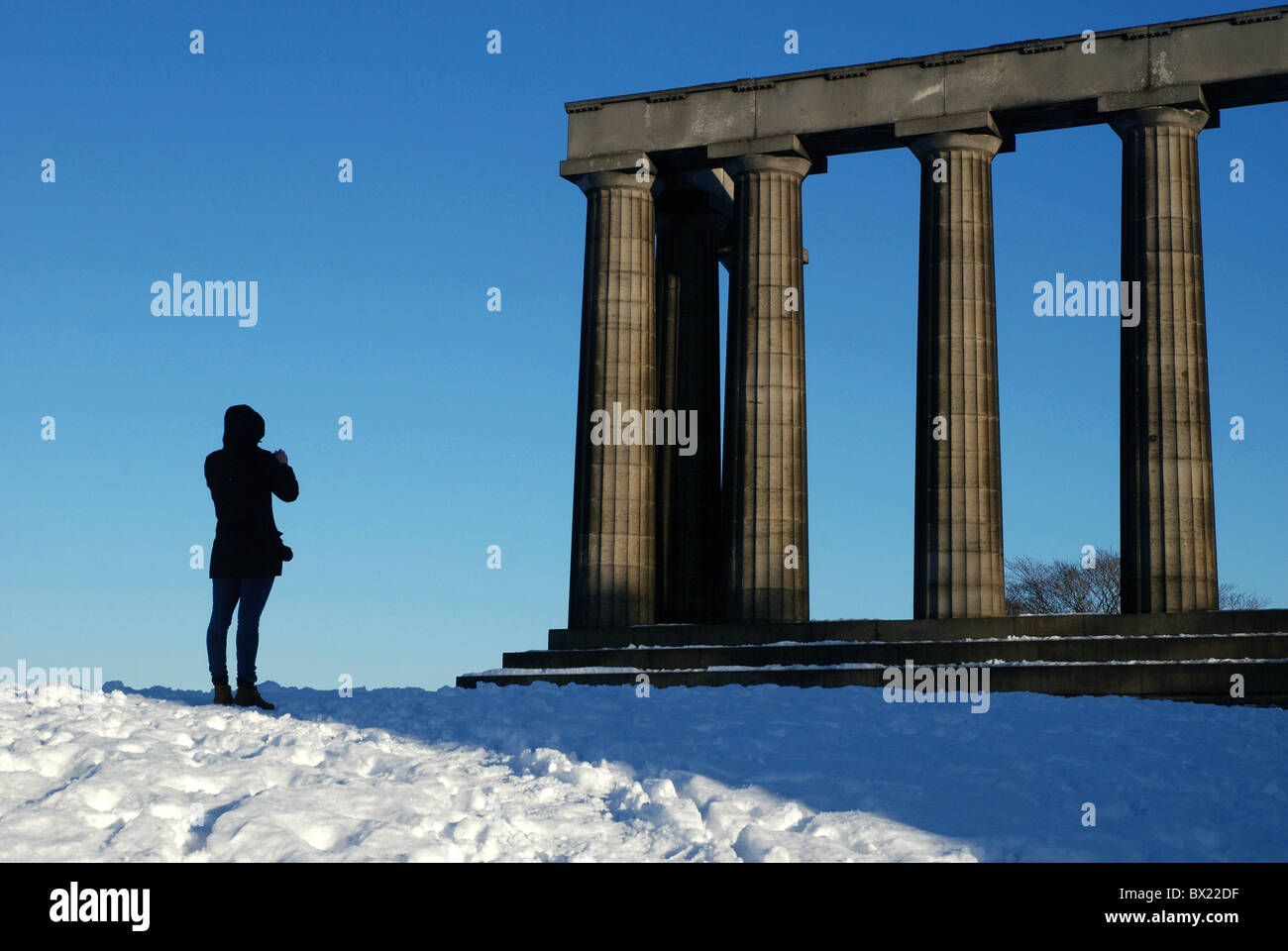 Un turista scattare fotografie del Monumento Nazionale su Calton Hill, Edimburgo, Scozia, Regno Unito dopo una caduta di neve. Foto Stock