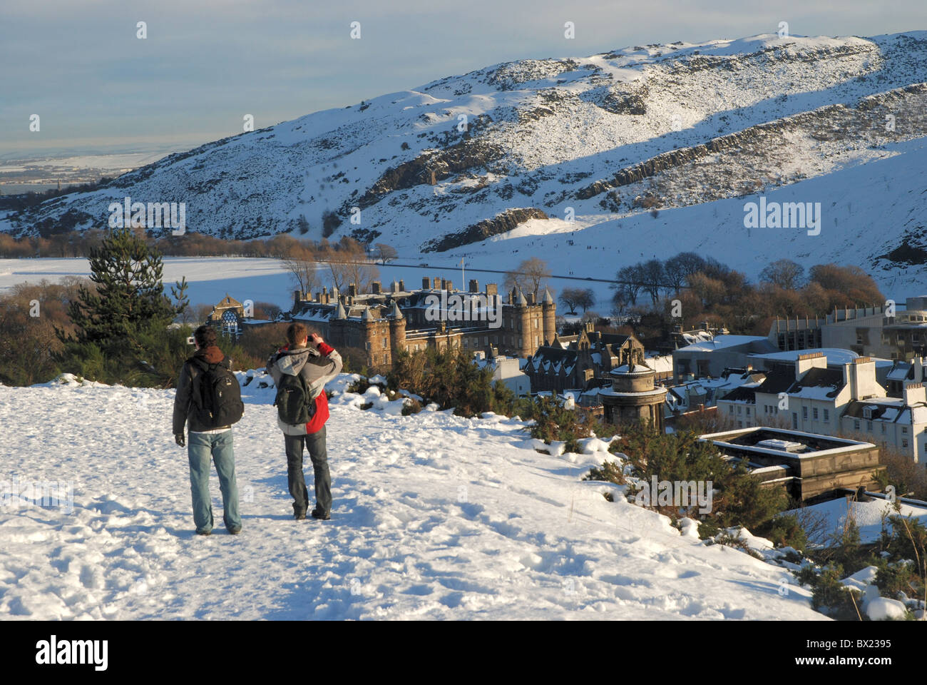 Due turisti camminando su un snowy Calton Hill a Edimburgo e fotografare la vista verso il Palazzo di Holyrood. Foto Stock