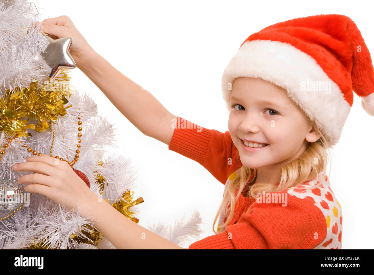 Foto di felice ragazza in Santa cap guardando la fotocamera mentre la decorazione di Nuovo Anno Albero Foto Stock