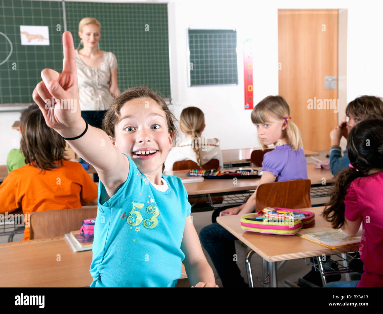 Ragazza giovane nella classe sollevando il dito Foto Stock