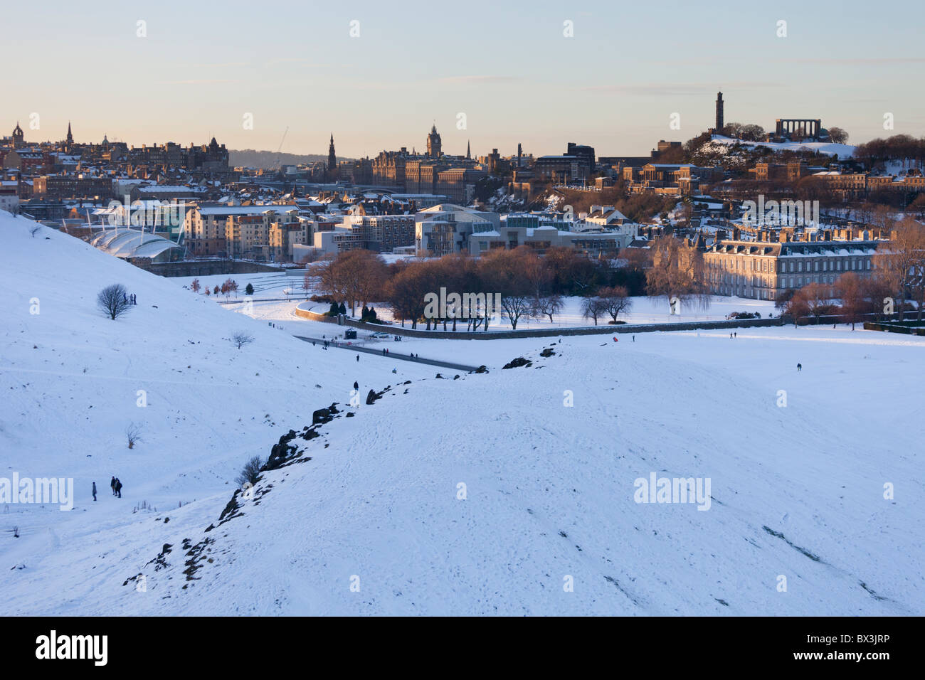 Snowy Holyrood Park, Edimburgo, con il Palazzo di Holyrood e Calton Hill al tramonto. Foto Stock