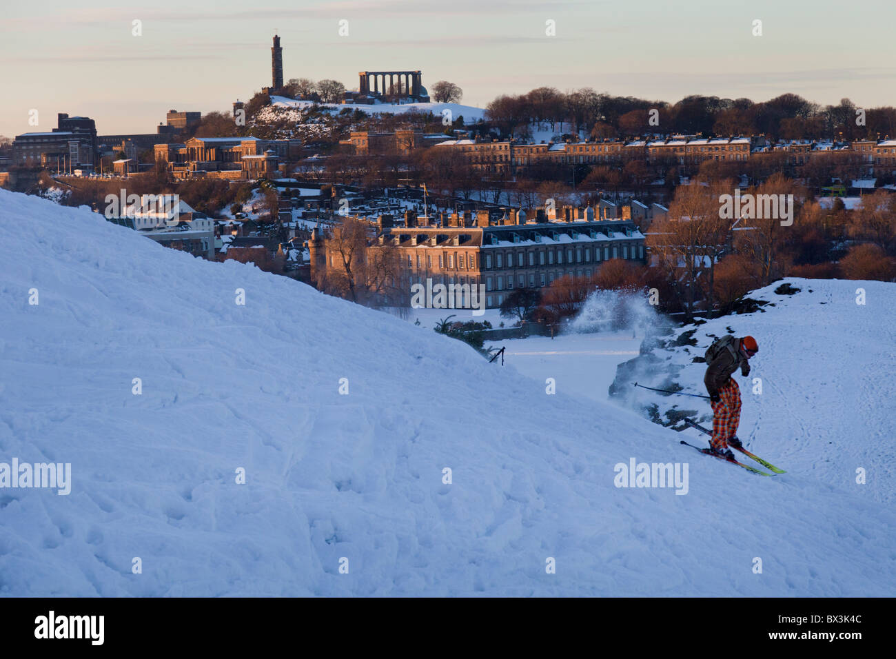 Sciatore in snowy Holyrood Park, Edimburgo, con il Palazzo di Holyrood e Calton Hill al tramonto. Foto Stock