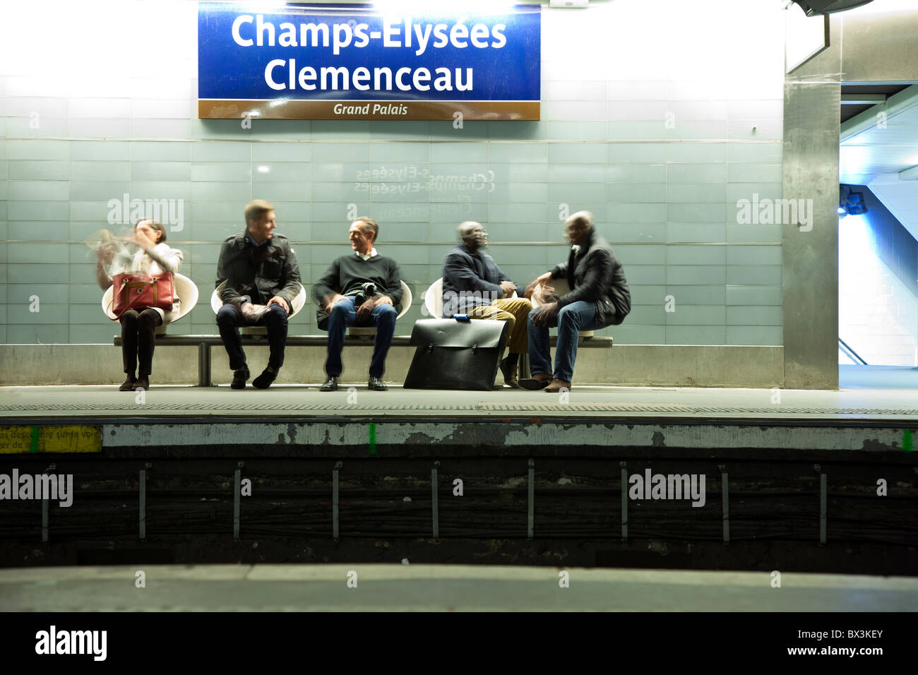 Gente seduta sul banco di lavoro, usando il telefono cellulare e in attesa per il treno nella stazione della metropolitana Champs Elysées Clemenceau a Parigi, Francia Foto Stock