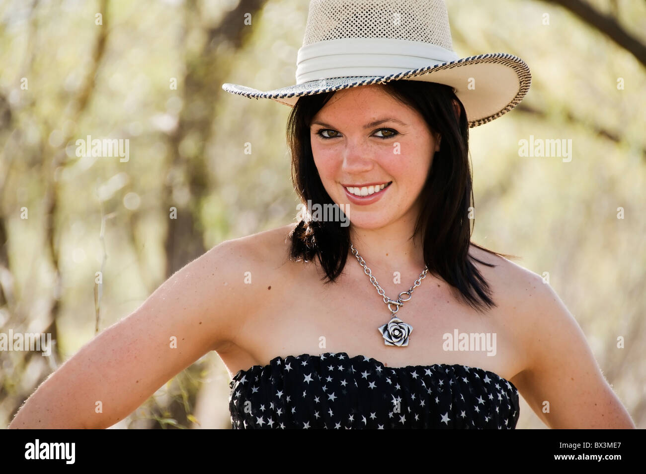 Testa e spalle vista di una bella bruna giovane donna che indossa un abito senza spalline e western hat sorridente alla fotocamera. Foto Stock