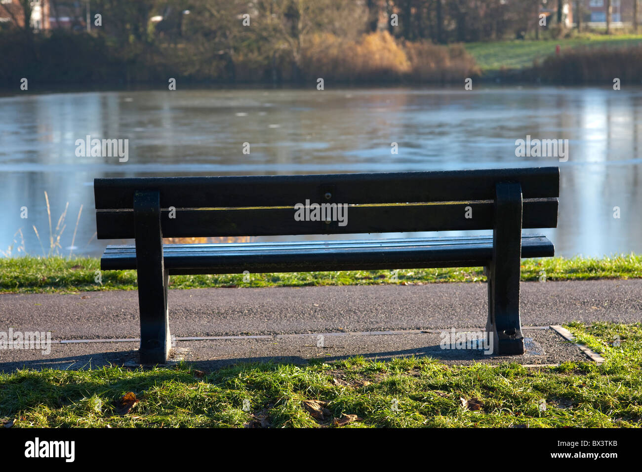 Lone vuoto una panchina nel parco di sole con lago ghiacciato in background Foto Stock