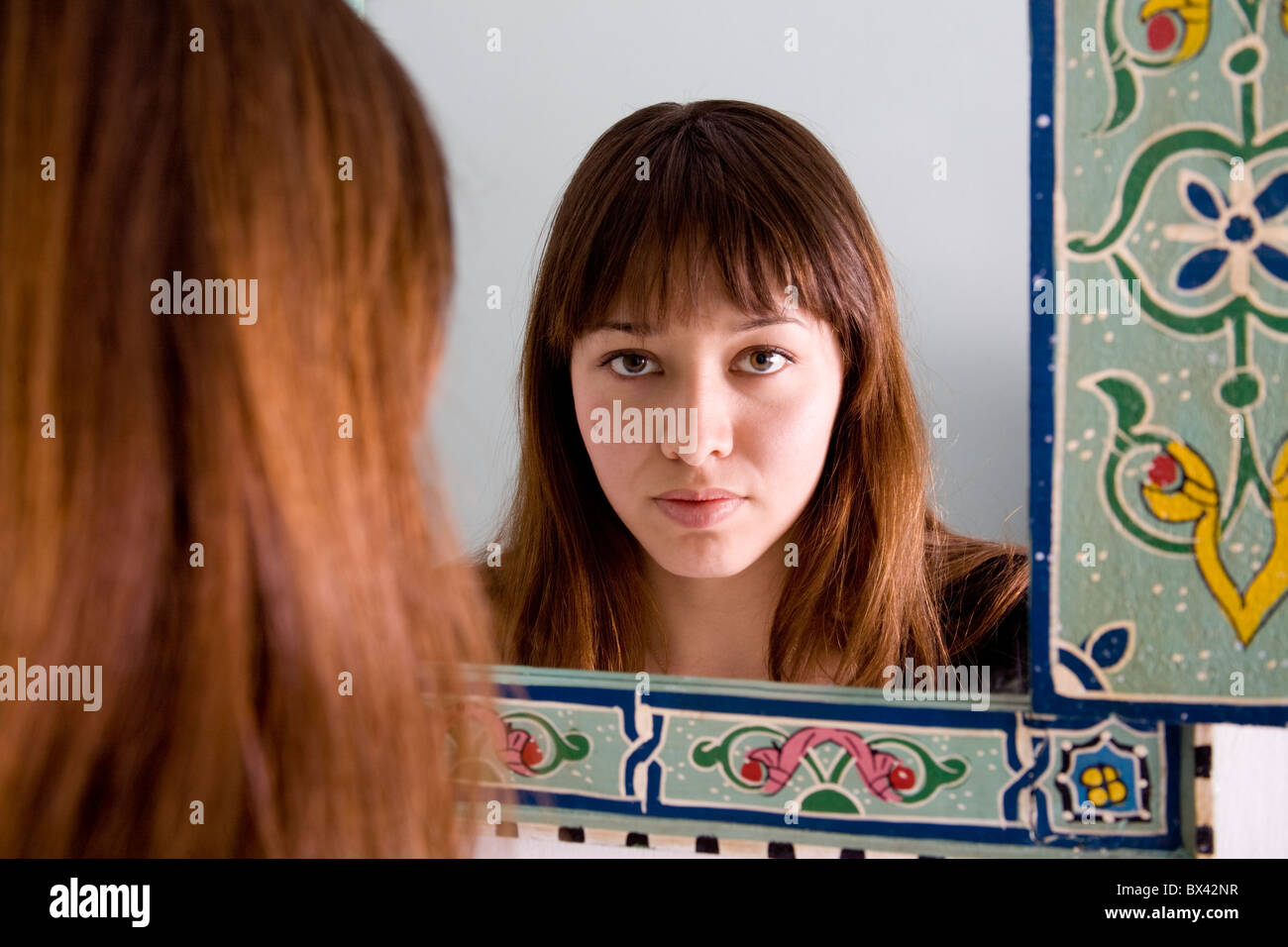Attraente giovane donna visto come un riflesso in un stile etnico specchio, con un grave aspetto sul suo viso Foto Stock