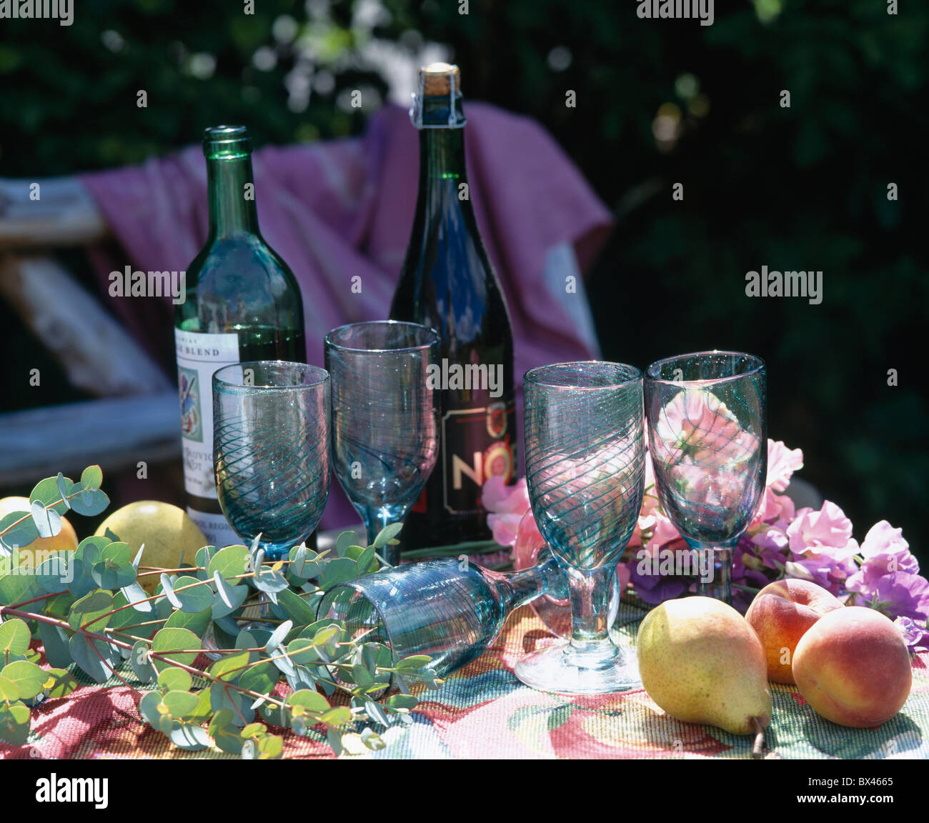 Still-Life di bottiglie di vino e di blu pallido-vino bicchieri sul tavolo da giardino con le pesche e le pere e fogliame Foto Stock