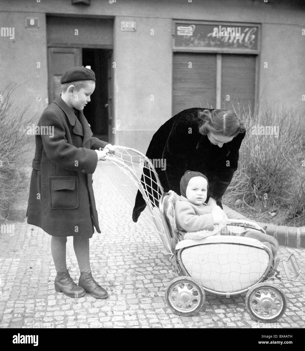 Praga, 1950. La madre aiuta il bambino nel passeggino. In background parrucchiere è chiusa.CTK Vintage foto Foto Stock