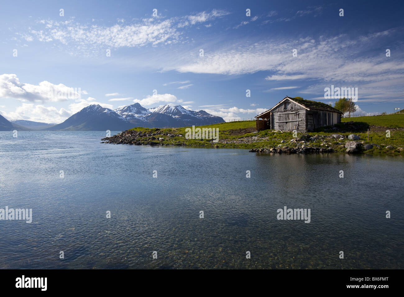 Cabina con tradizionale tetto in erba che si affaccia su un fiordo e montagne innevate nella penisola di Lyngen, Troms County, Norvegia Foto Stock