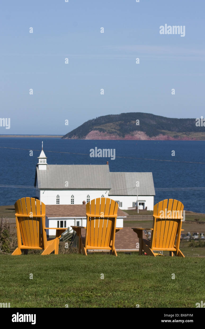 Giallo Adirondack sedie con vista chiesa su un isola nel Golfo di San Lorenzo, Iles de la Madeleine, Quebec, Canada Foto Stock