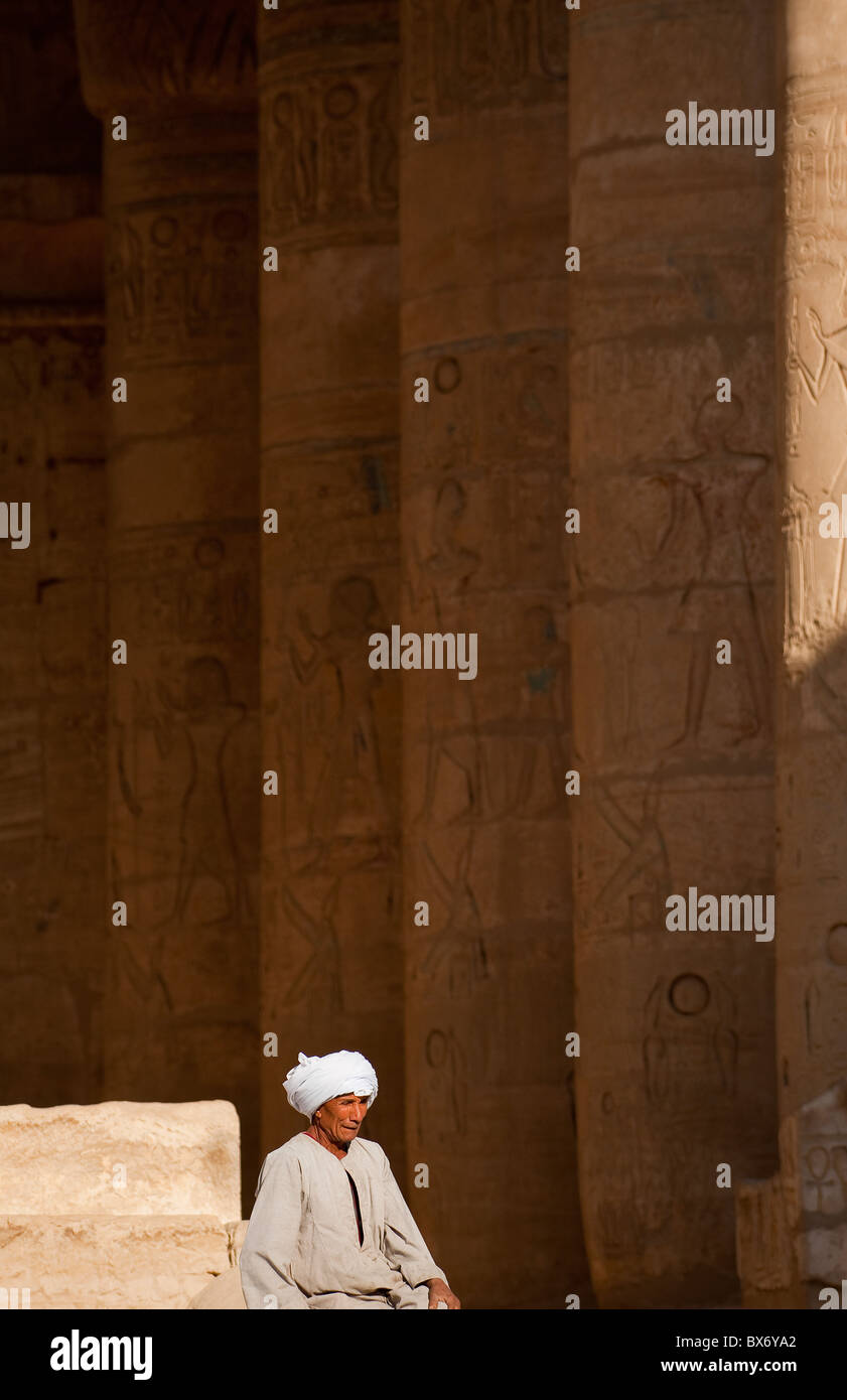 Un solitario uomo egiziano in abito tradizionale udienza e girovagare per i pilastri della rovina del tempio egiziano di Ramses II Foto Stock