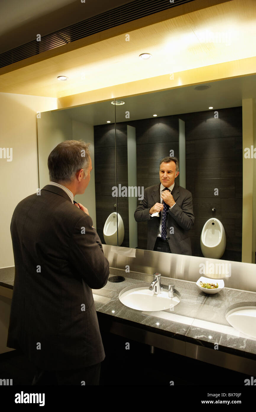 Imprenditore fiducioso nella parte anteriore dello specchio bagno/wc pubblico Foto Stock