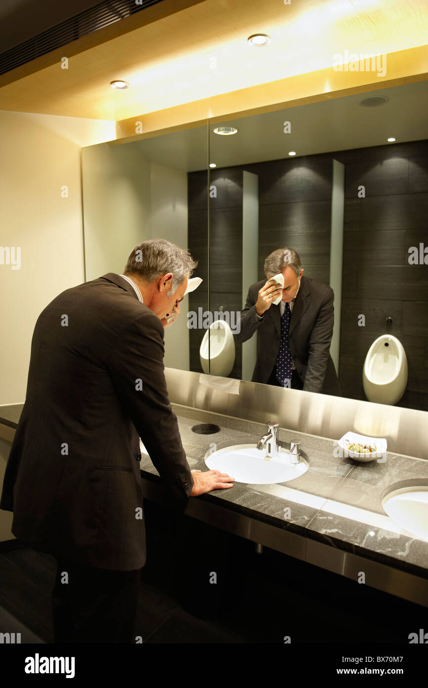 Imprenditore ansioso di fronte a uno specchio in bagno/wc pubblico Foto Stock