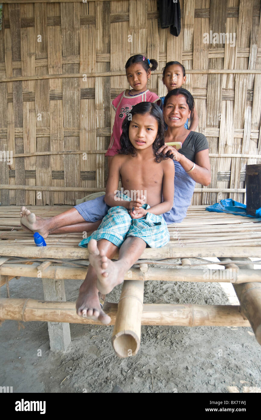 Mishing tribeswoman pettinatura di sua figlia i capelli sulla veranda della loro casa di famiglia, Majuli Island, Assam, India, Asia Foto Stock