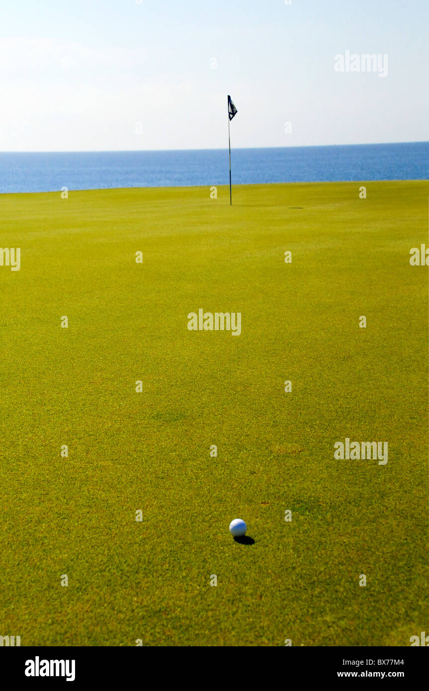 Palla da golf sul putting green con bandiera pole e Oceano Pacifico a Puerto Los Cabos Golf Club di San Jose del Cabo, Messico Foto Stock