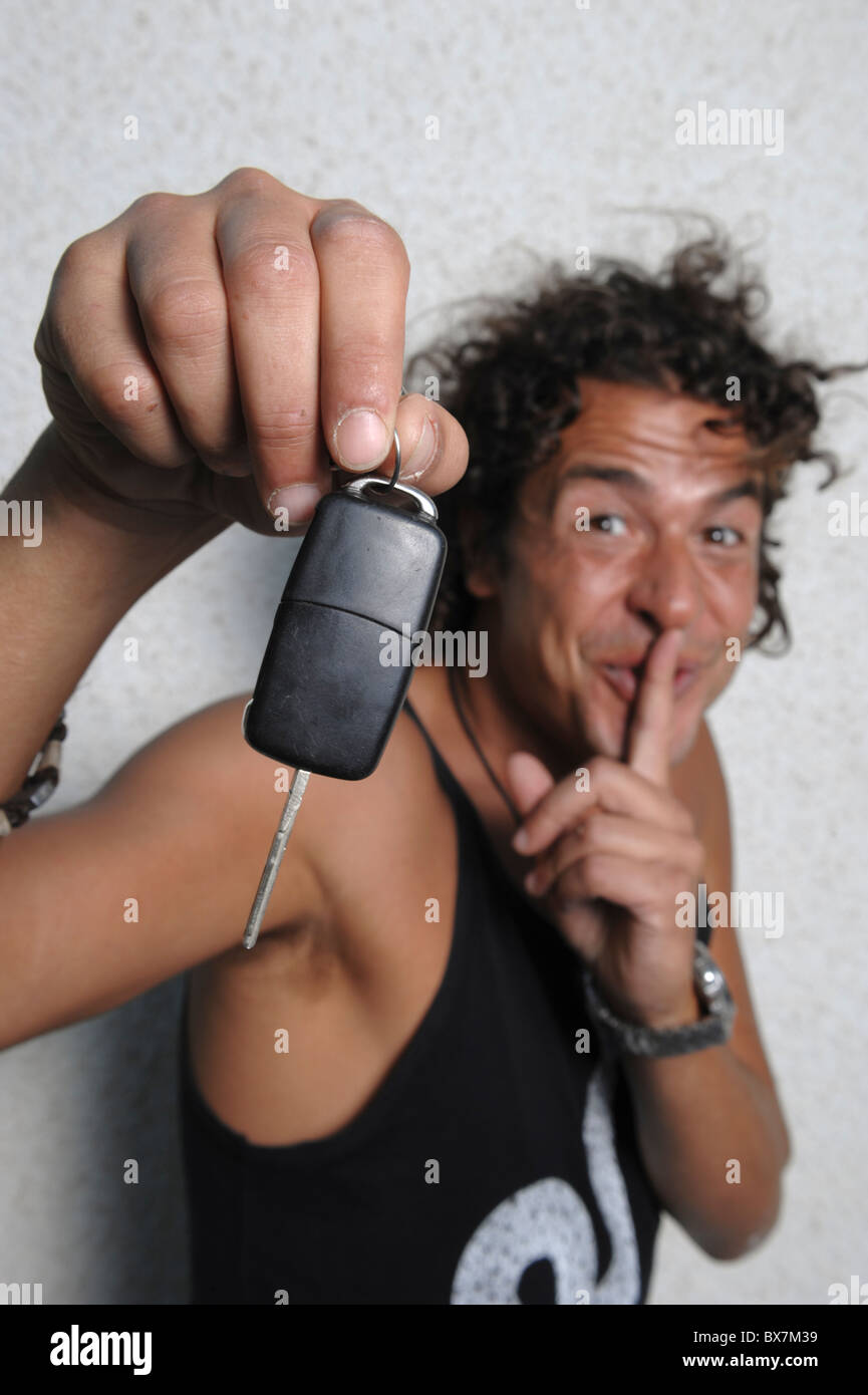Giovane uomo in possesso di una chiave auto e facendo un gesto shush con il suo dito contro le sue labbra Foto Stock