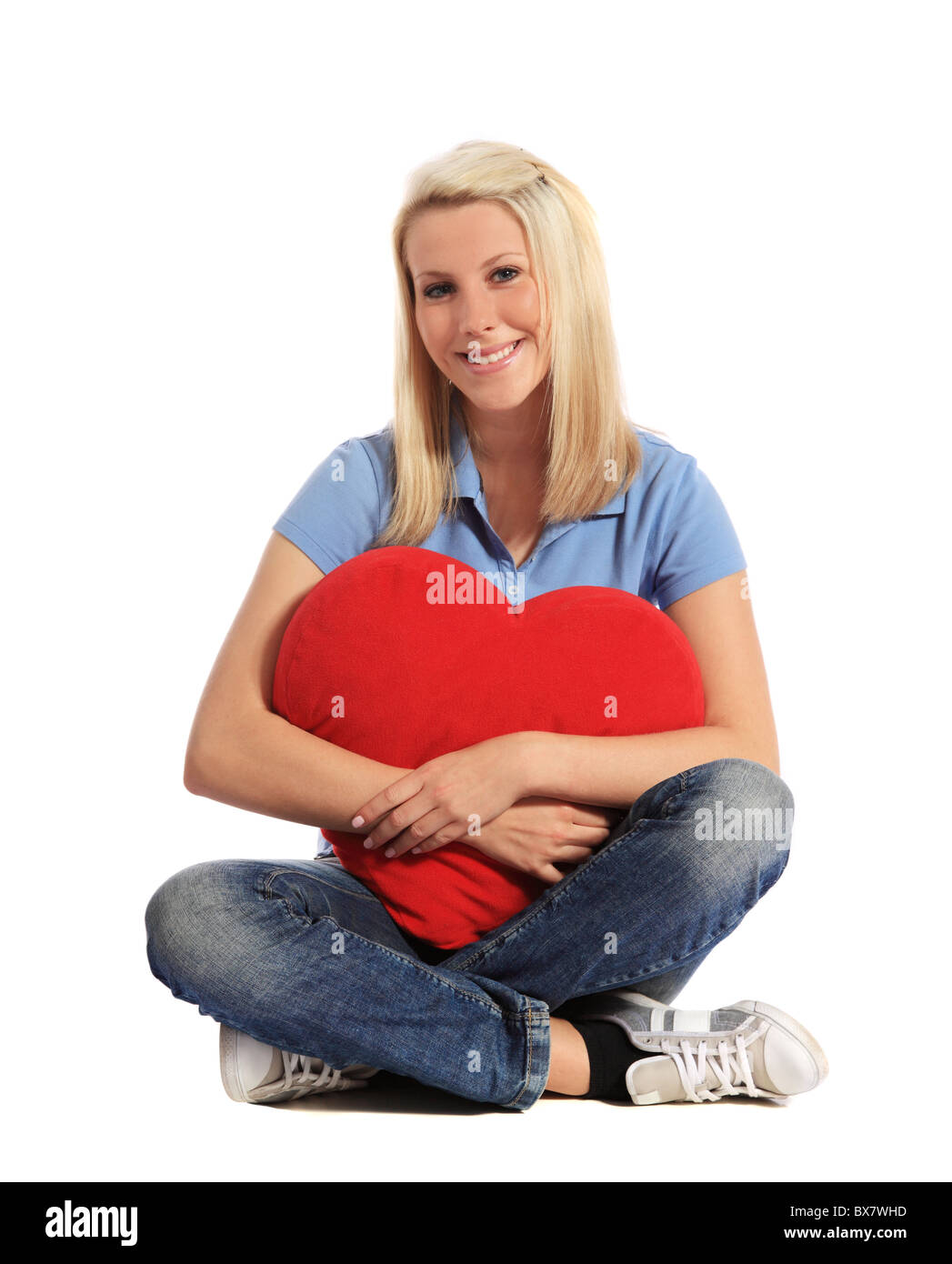 Attraente giovane donna abbracciando una a forma di cuore cuscino. Tutto su sfondo bianco. Foto Stock