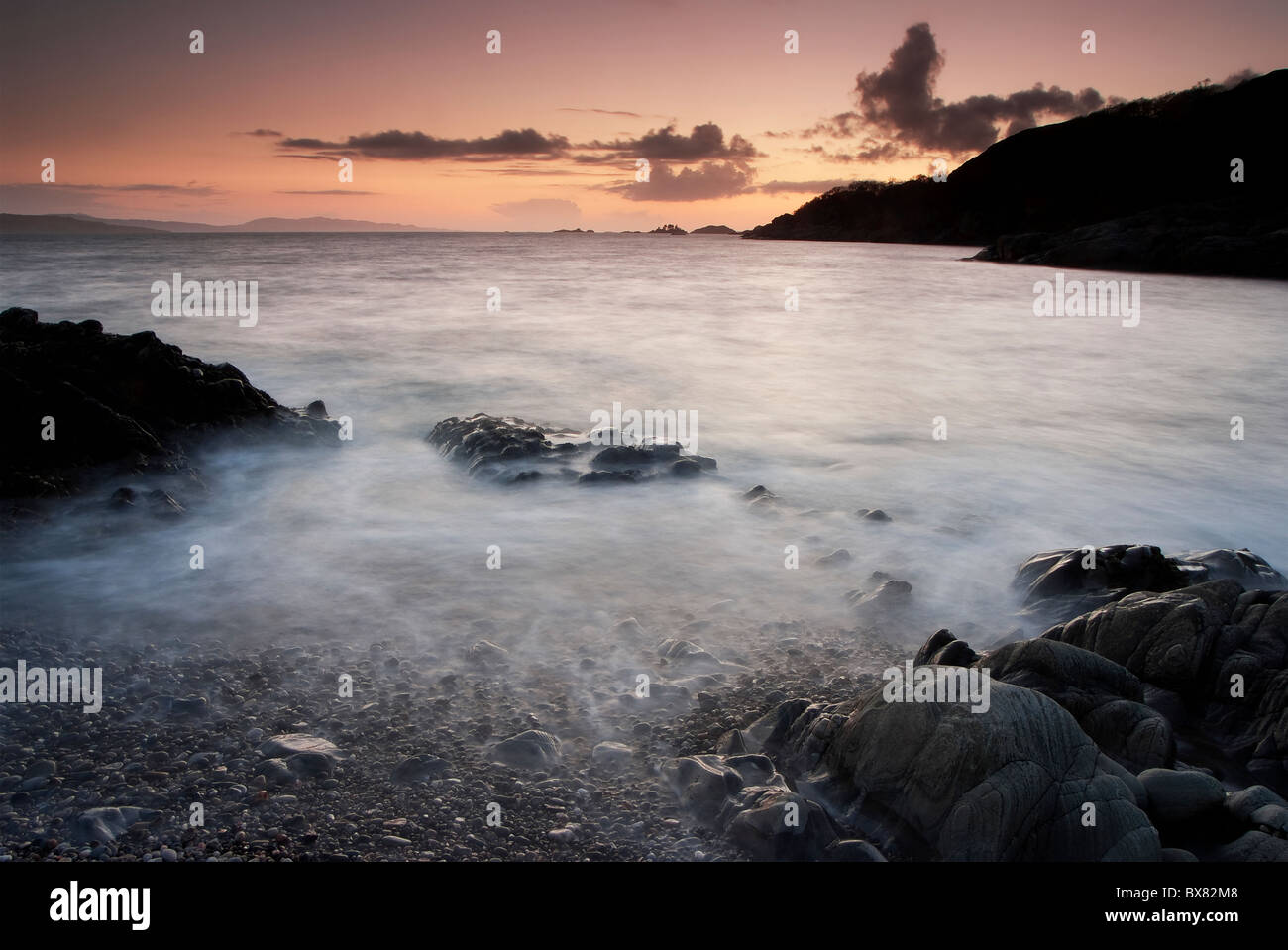 Onde che si infrangono su una rocciosa spiaggia di ghiaia al tramonto durante una lunga esposizione creando splendide e immagini mistiche di Scozia Foto Stock