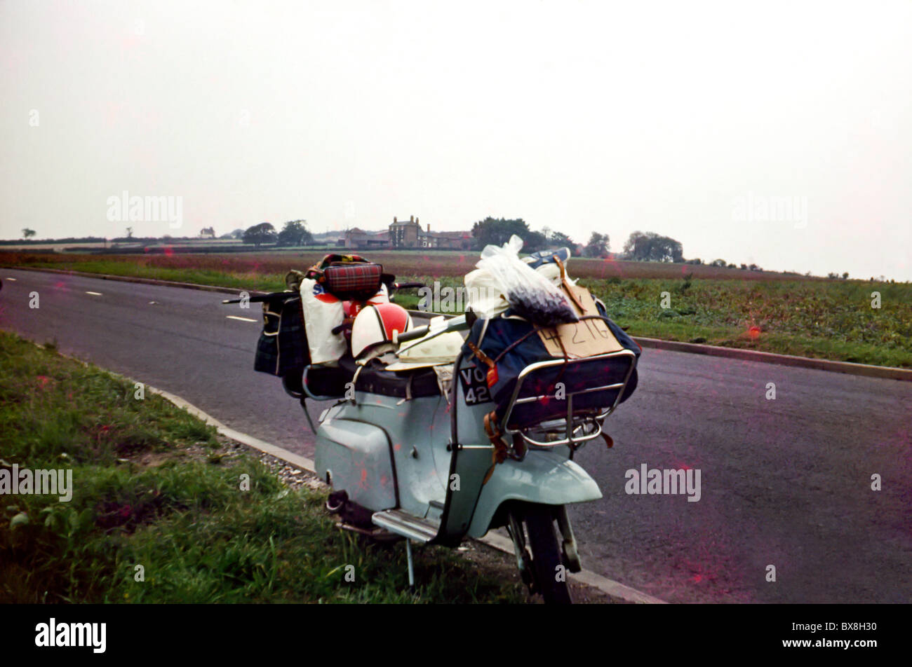 Original 60'simmagine di uno scooter/ciclomotore parcheggiato fino a lato della strada nel paese. Lo scooter è carico di bagagli. Foto Stock