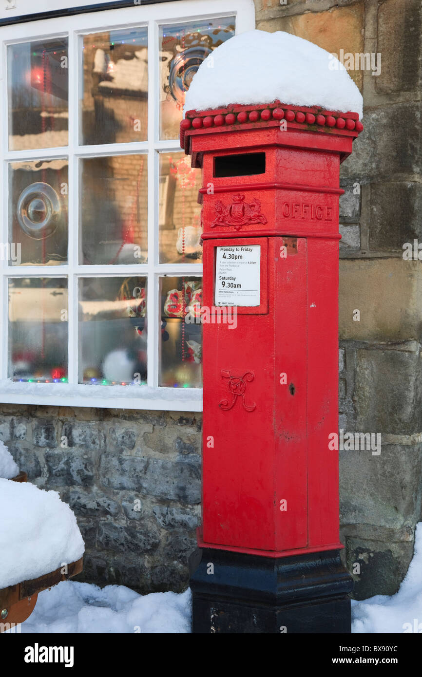 Old red Victorian postbox al di fuori del post office con la neve in inverno. Hartington, Derbyshire, Inghilterra, Regno Unito, Gran Bretagna. Foto Stock