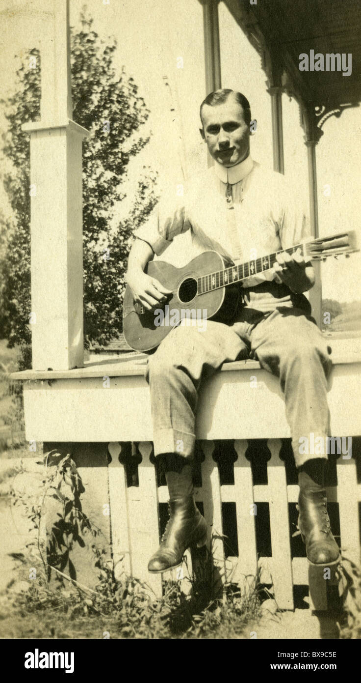 Uomo seduto sulla veranda in legno a suonare la chitarra durante gli anni venti anni trenta musicisti folk music americana in bianco e nero Foto Stock
