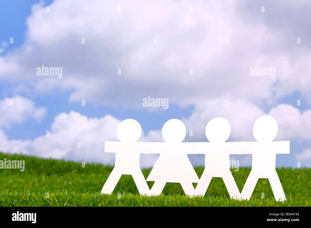 Concetto di immagine del popolo di carta tenendo le mani in un campo con un cielo blu sullo sfondo. Foto Stock