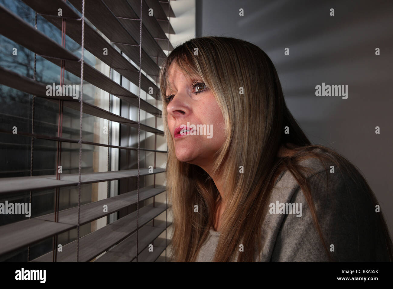 Donna che guarda fuori da una finestra attraverso un cieco Foto Stock