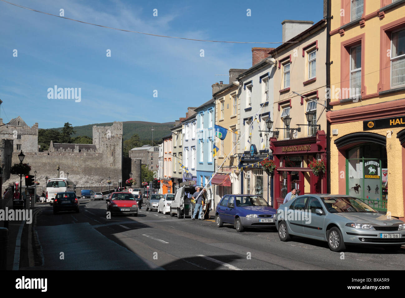 Una vista lungo una sfilata di colorati negozi sulla strada del Castello di Cahir verso il Castello di Cahir, Co Tipperary, Irlanda (Eire). Foto Stock