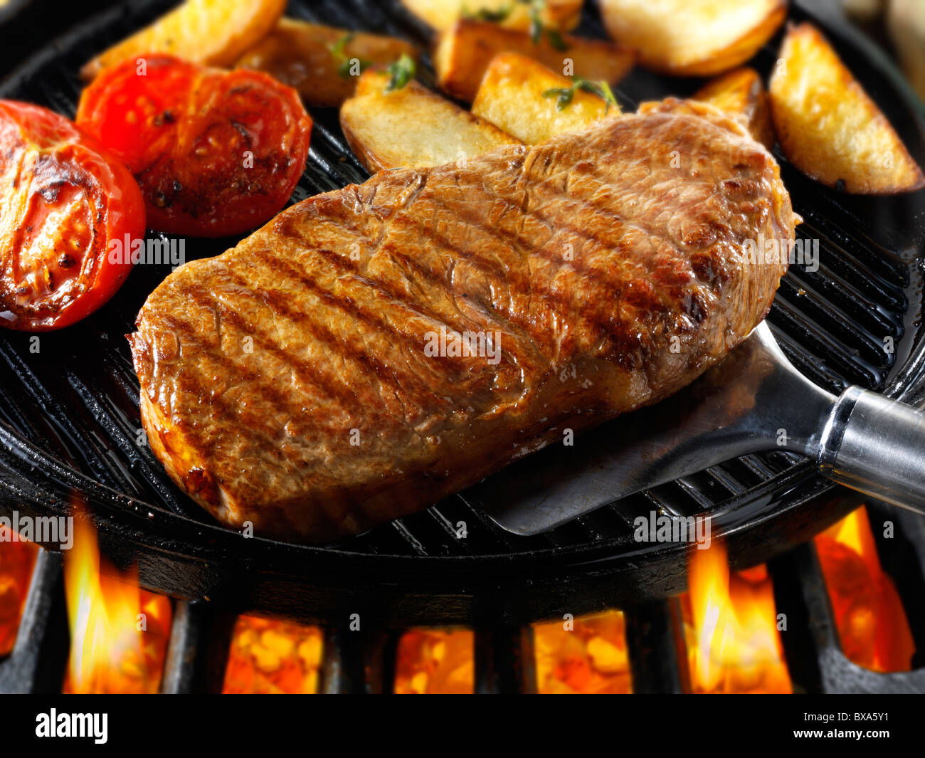 Lombata di manzo bistecche , i pomodori e patatine fritte in padella fritto su un barbecue. Alimenti a base di carne le foto, foto e immagini. Foto Stock