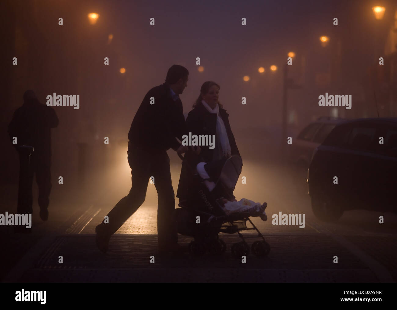 Fitta nebbia avvolge il centro della città di Ely nel Cambridgeshire. È presto la sera e un paio con il passeggino sono fuori a piedi. Foto Stock Fitta nebbia avvolge il centro della città di Ely nel Cambridgeshire. È presto la sera e un paio con il passeggino sono fuori a piedi. Foto Stock
