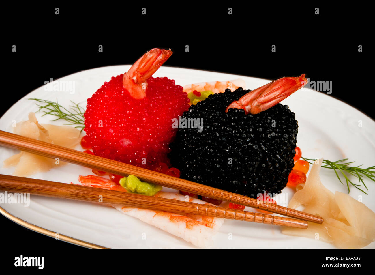 Il nigiri sushi coperto di rosso e nero uova di pesce con wasabi e zenzero. Con due bastoncini. Sul nero. Foto Stock