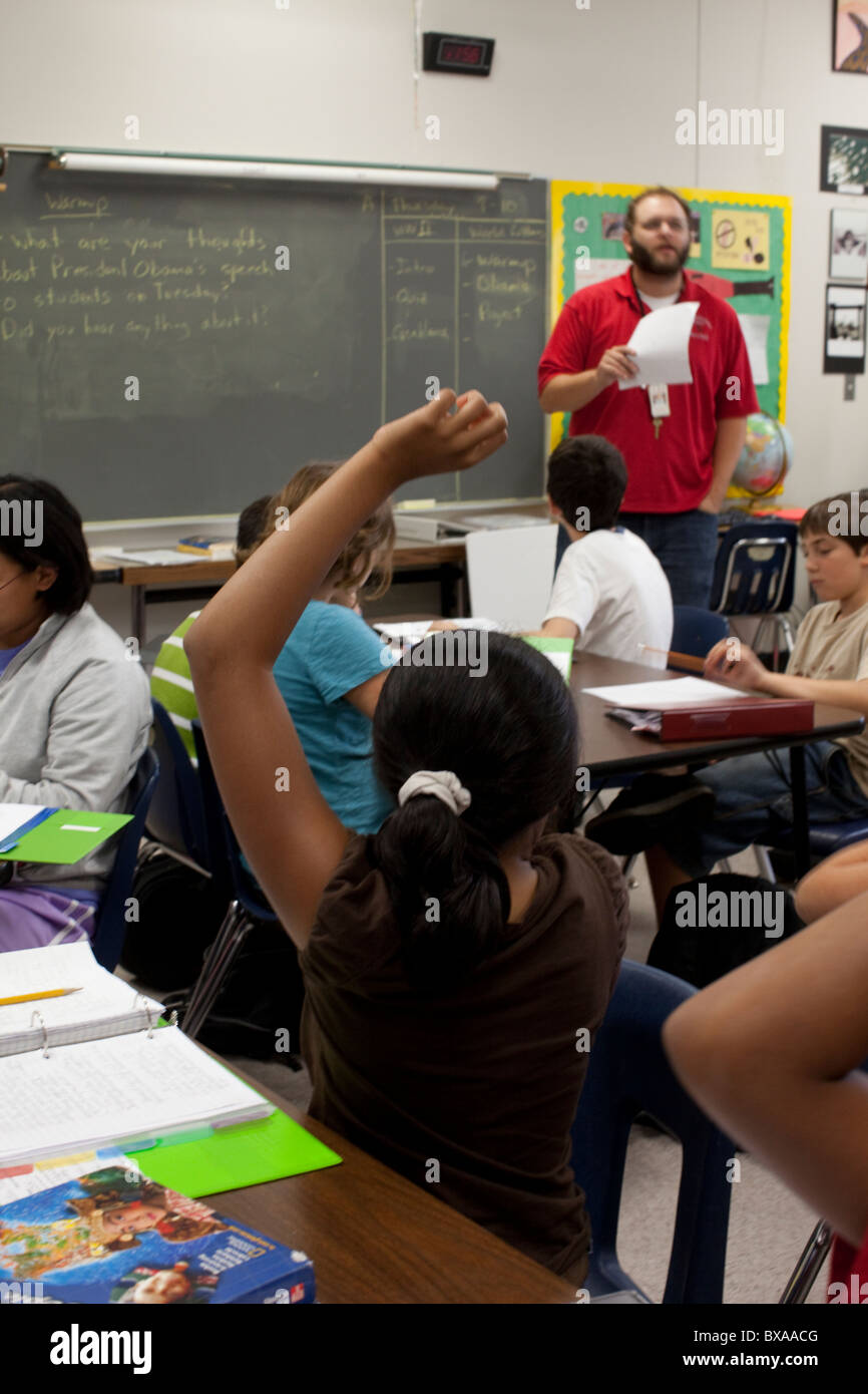 Sesto-grade ragazza solleva la mano in risposta a maschio dell'insegnante in questione studi sociali classe nel centro aula scolastica di Austin Foto Stock
