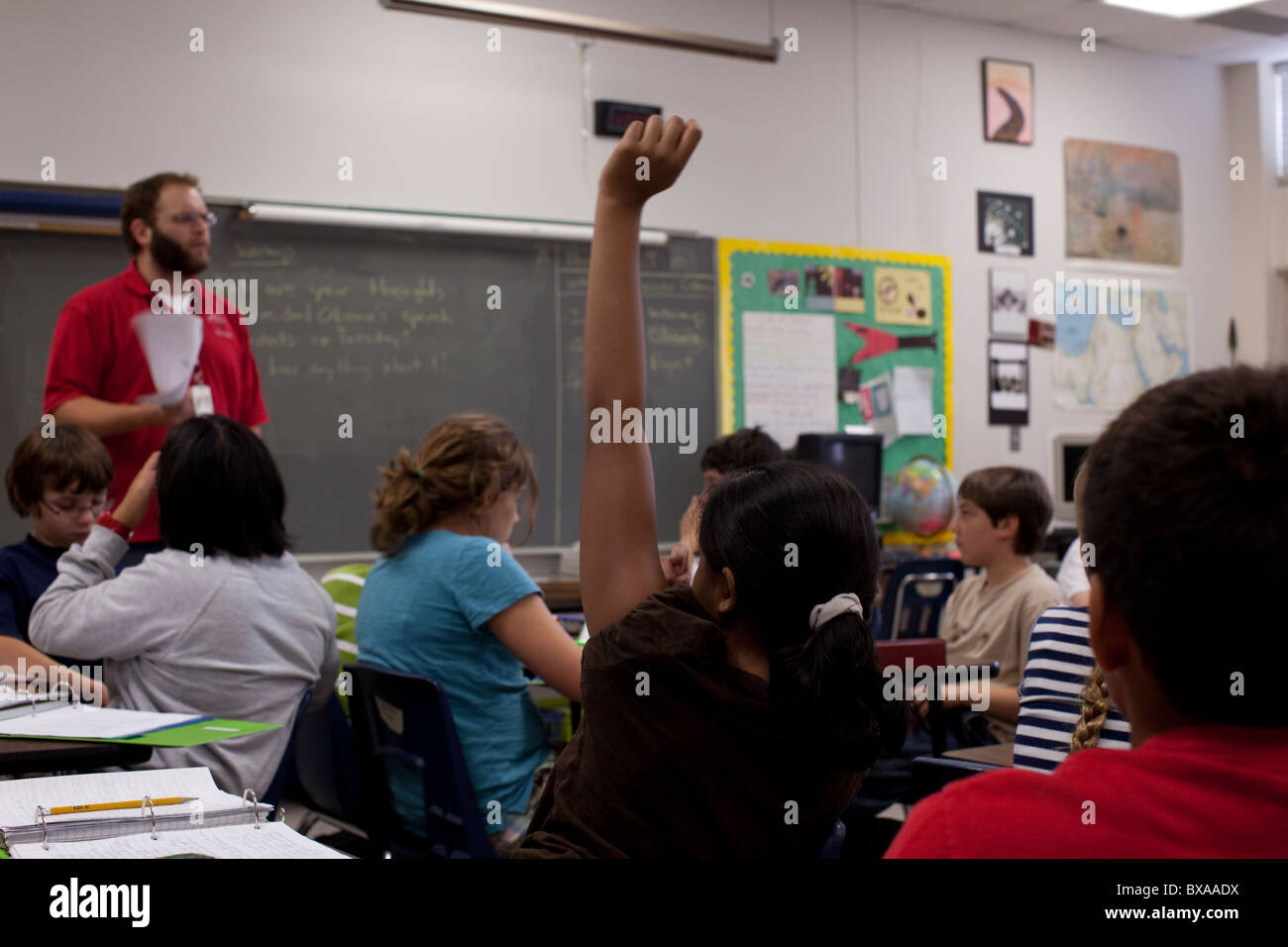 Sesto-grade ragazza solleva la mano in risposta a maschio dell'insegnante in questione studi sociali classe nel centro aula scolastica di Austin Foto Stock