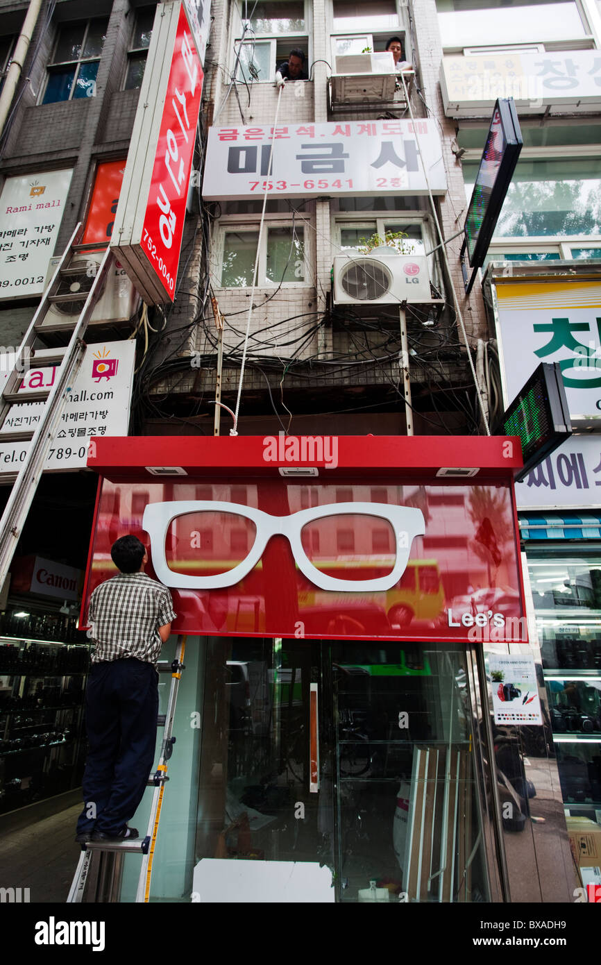 Lavoratore sta mettendo su un segno negozio nel quartiere degli affari di Seoul, Corea del Sud Foto Stock