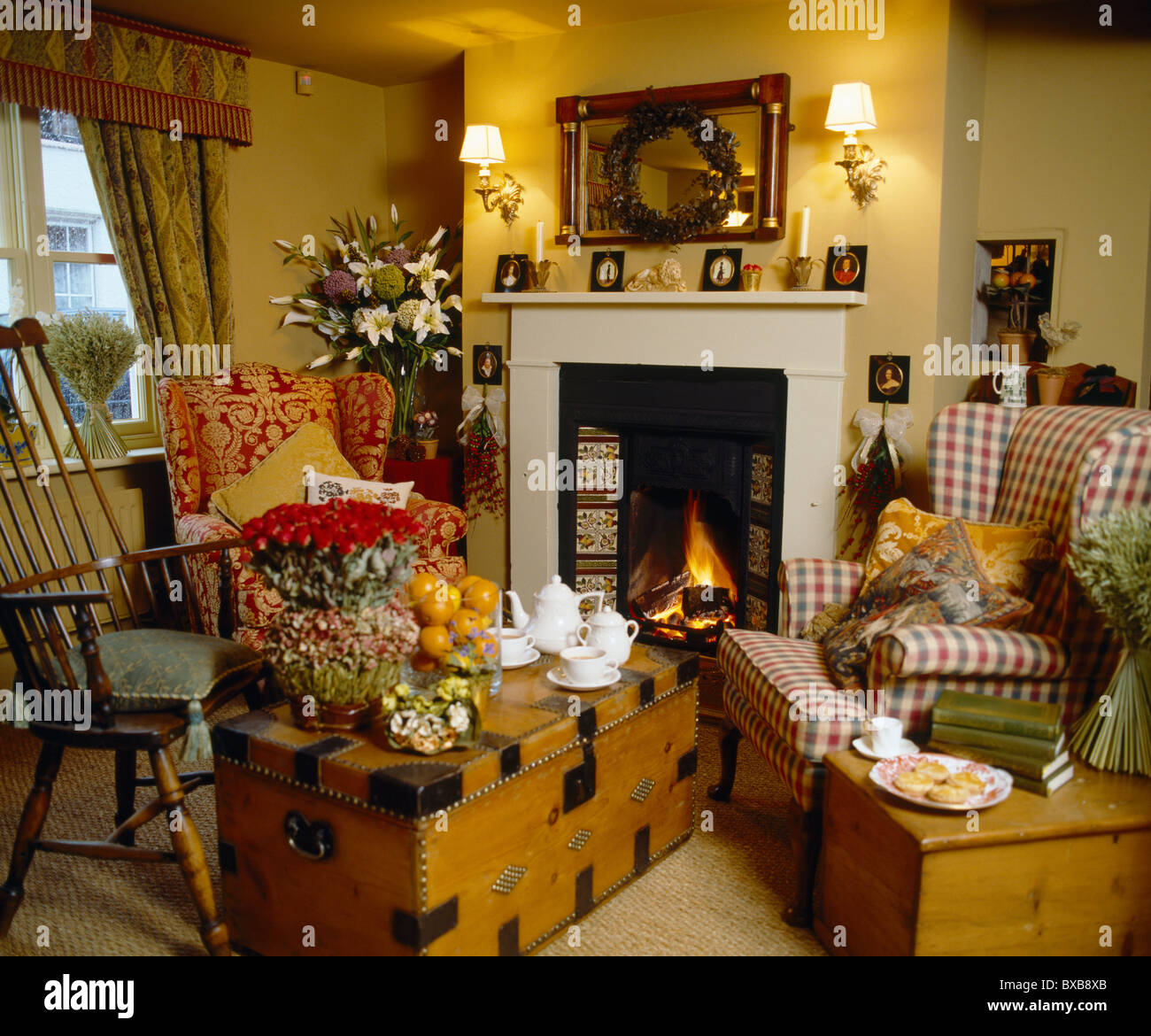 Poltrone di legno vecchio e il petto davanti al camino con fuoco illuminata in giallo cottage soggiorno con parete illuminata-luci Foto Stock