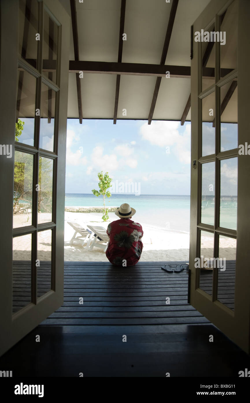 Uomo seduto sul legno decking in Maldive Foto Stock