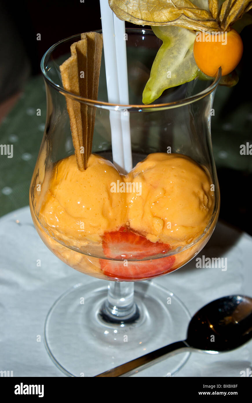 Congelati arancione sorbetto di frutta ricoperti in modo chiaro la grappa liquore dolce snifter calice con cialda croccante biscotto fragola guarnire Foto Stock