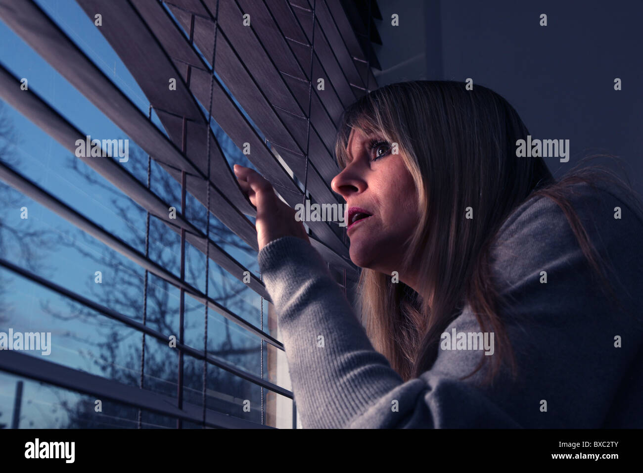 Preoccupato donna che guarda fuori da una finestra tenda alla notte. Foto Stock