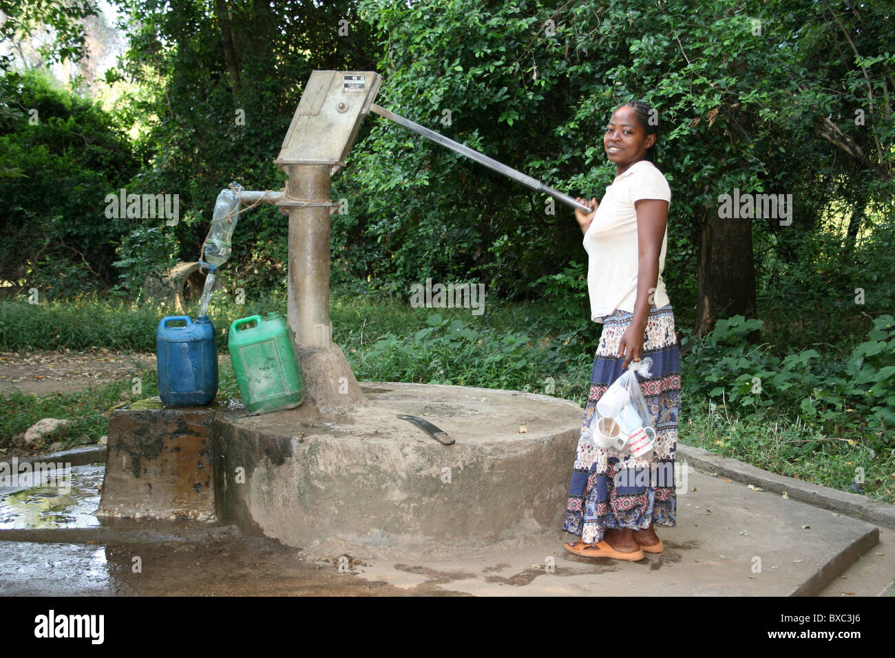 Sorridente donna etiope il pompaggio di acqua da un pozzo Foto Stock
