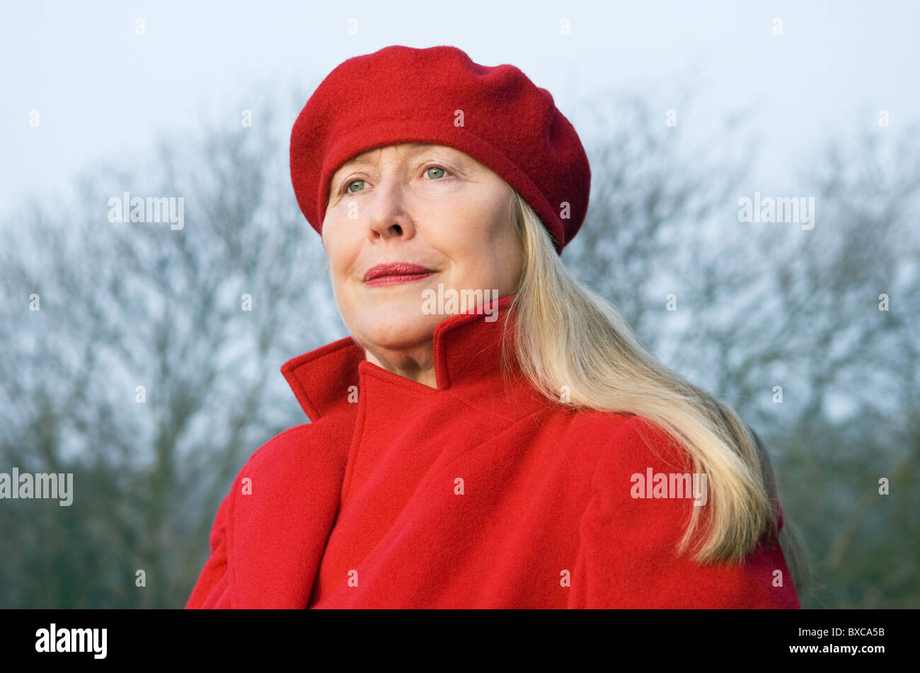 Una bella donna anziana nei suoi anni sessanta indossando un rosso cappotto e berretto. Foto Stock