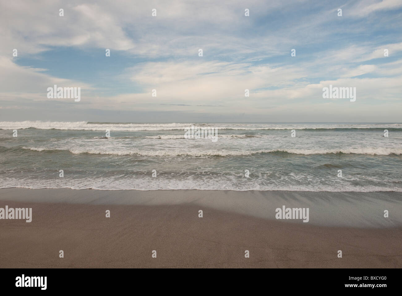 Onde che si infrangono sulla spiaggia sotto un nuvoloso cielo blu Foto Stock