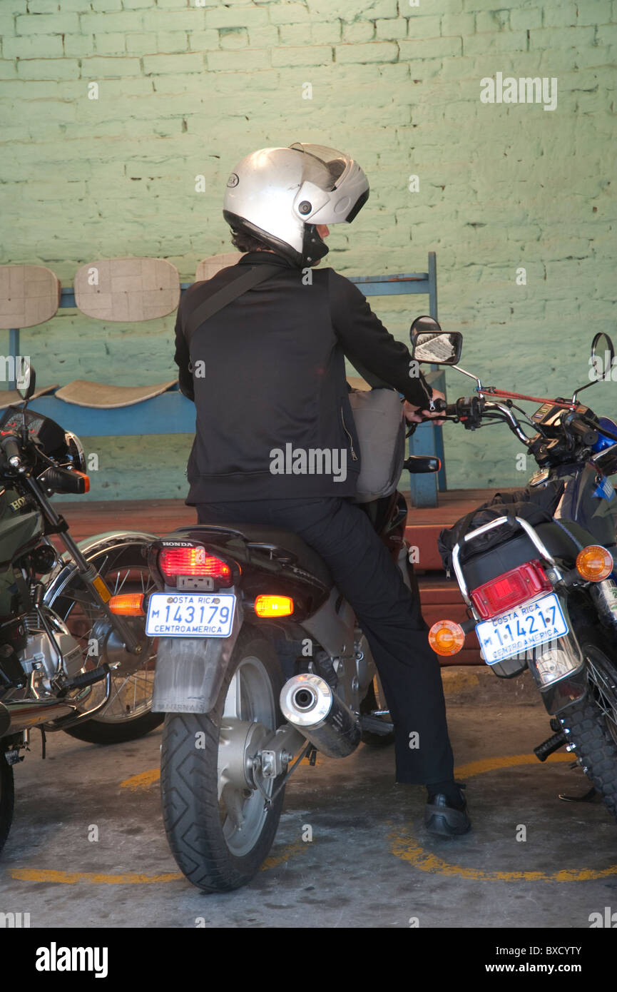 Parcheggiato motociclista indossando un nero business suit e un casco bianco, dalla parte posteriore Foto Stock